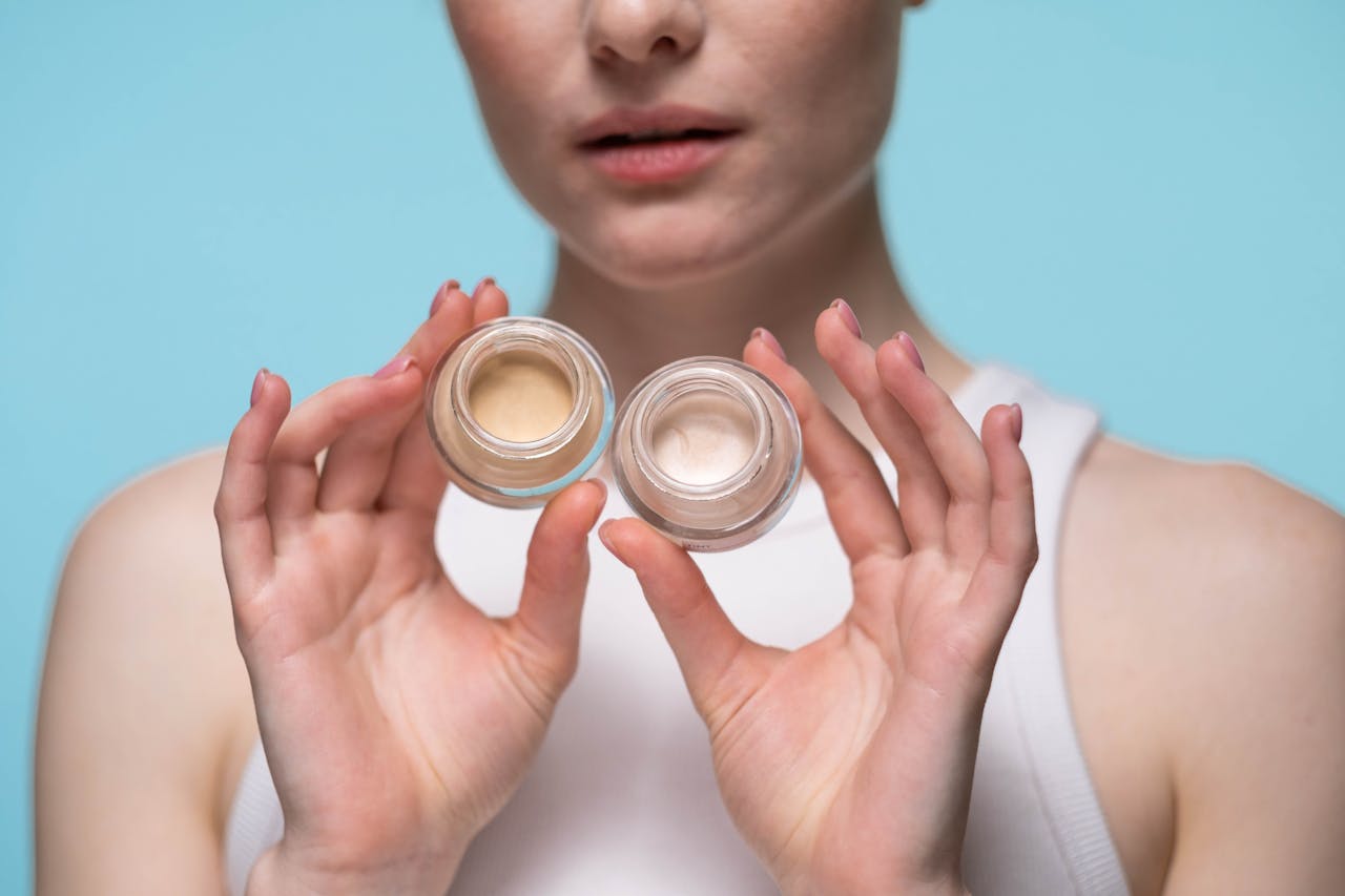 Close-up of a woman holding skincare jars against a blue background, showcasing beauty and self-care.